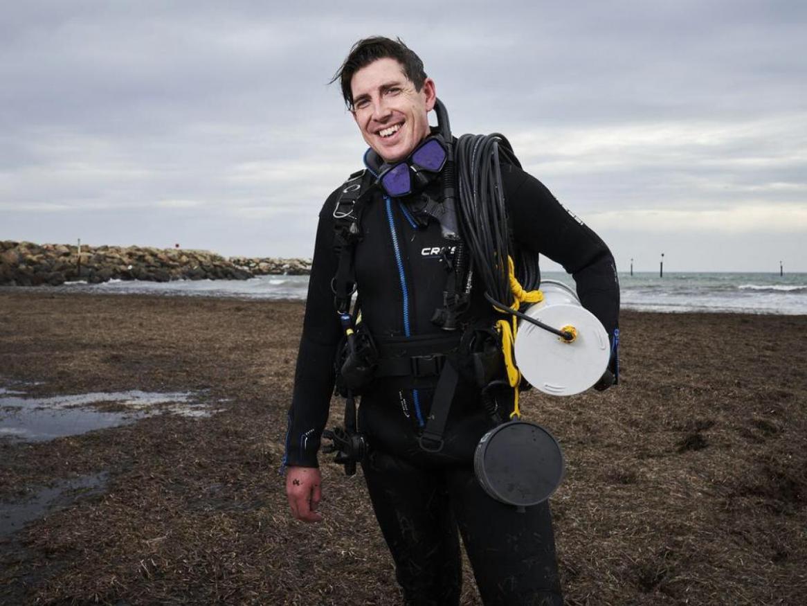 Dr Dominic McAfee, scientist, holding speaker on beach