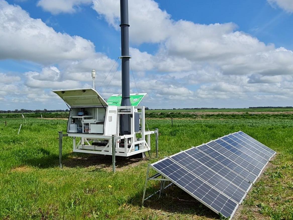 A weather detection instrument and solar panel are set up in a grassy field.