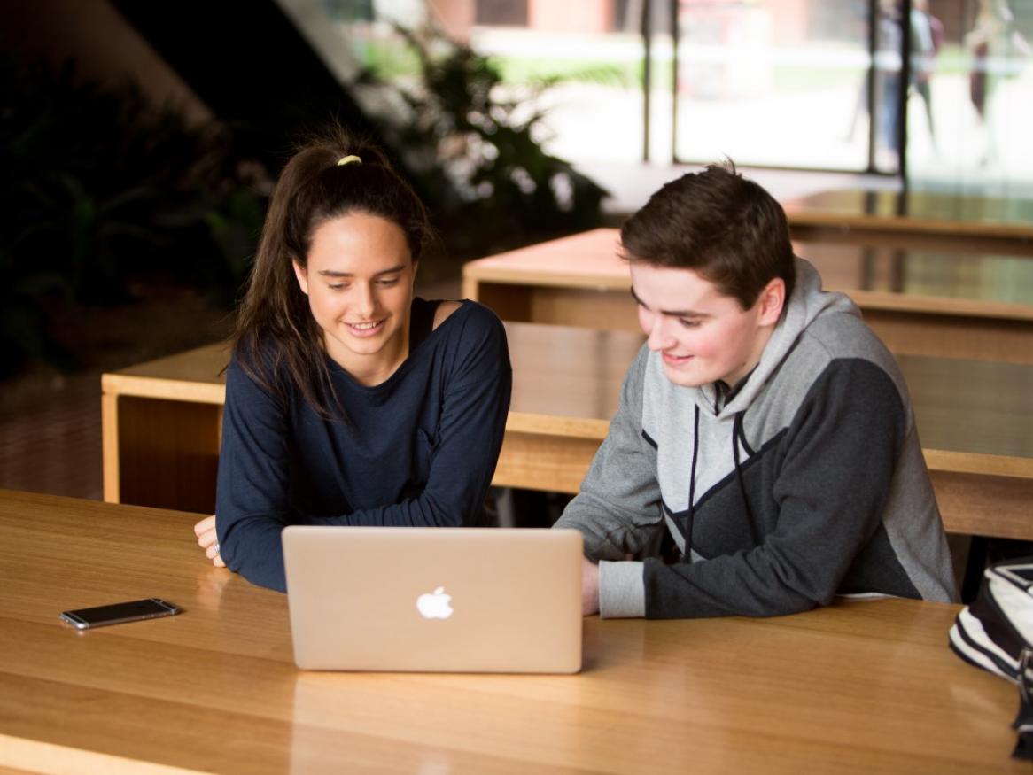 Two students sitting in front of an open laptop