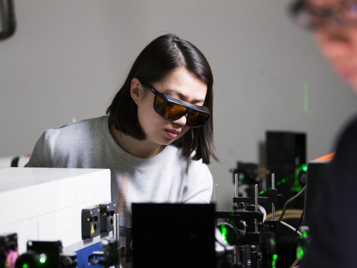 Research student wearing protective eye goggles, working with laser machinery