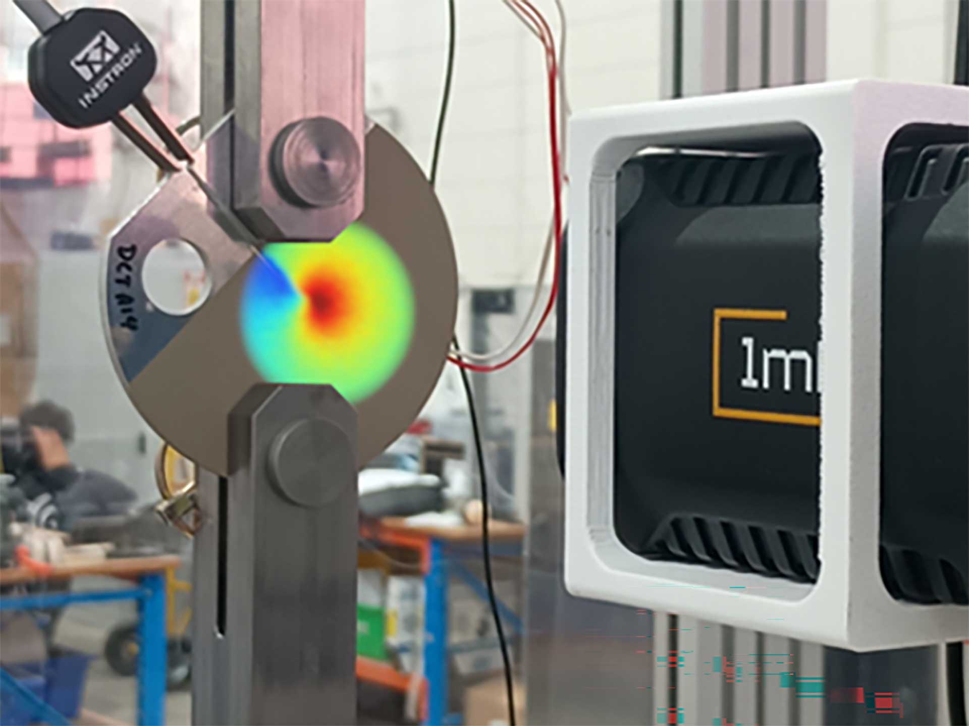A lab testing rig with a colorful strain map on a metal specimen