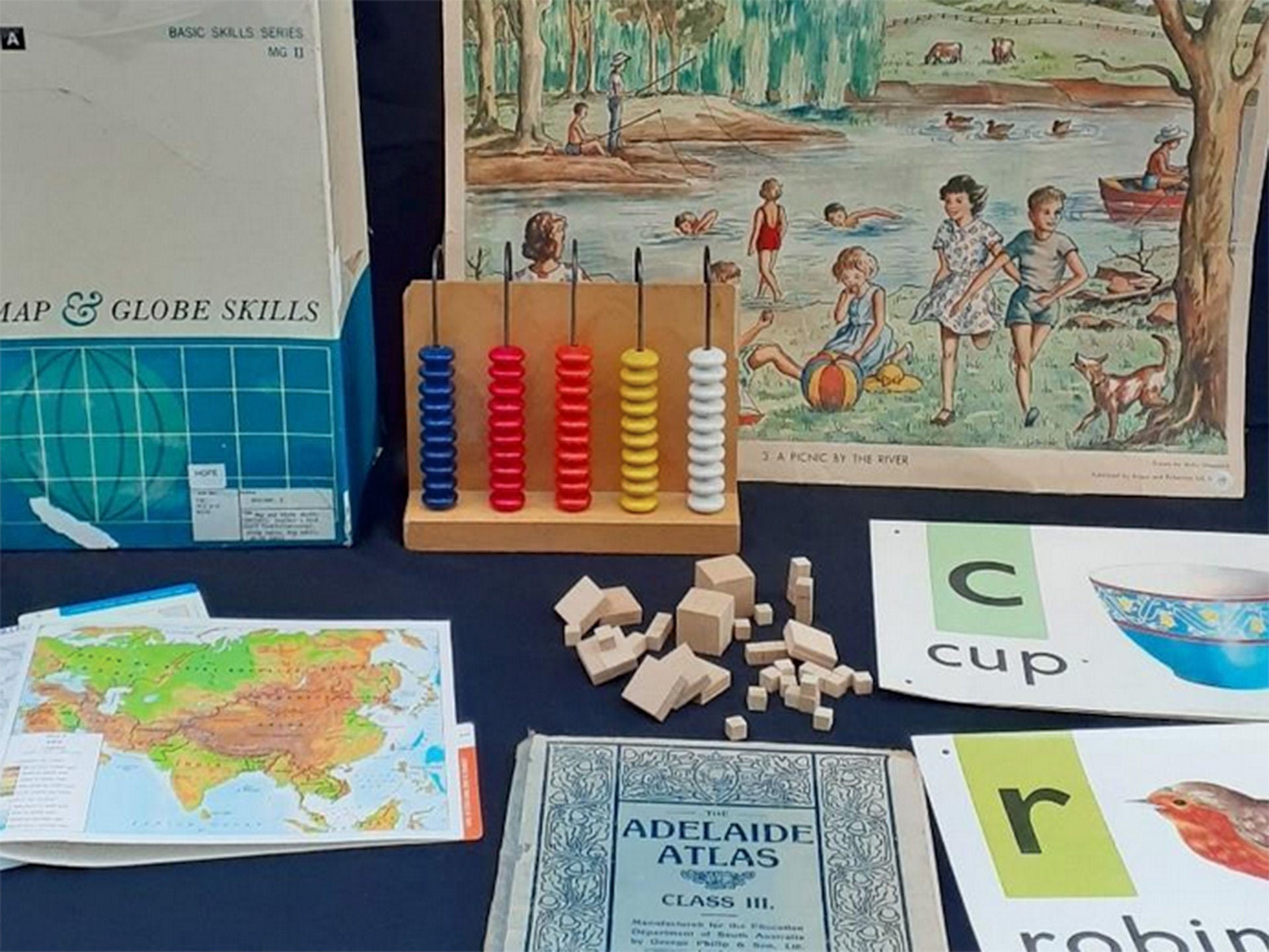 Various items from the History of Primary Education in South Australia Collection showing an aold Adelaide Atlas book, map, prompt cards with a picture of an item and the letter that it starts with and the name of the item. E.g. 'C' for Cup