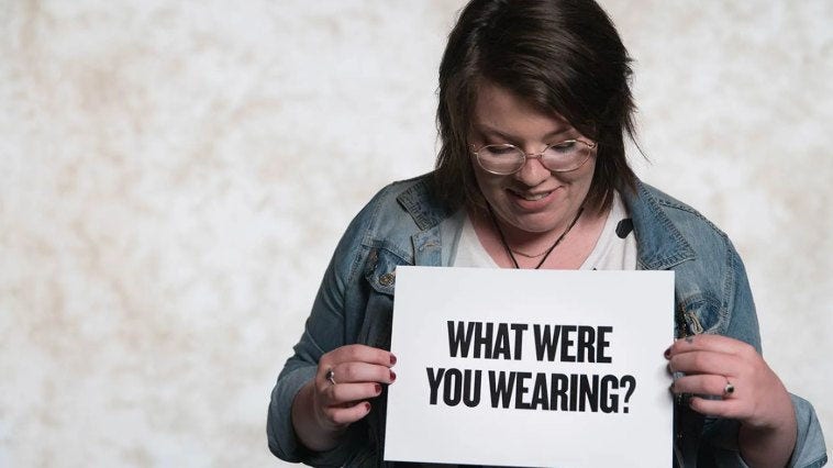 Woman holding a sign that says what were you wearing?