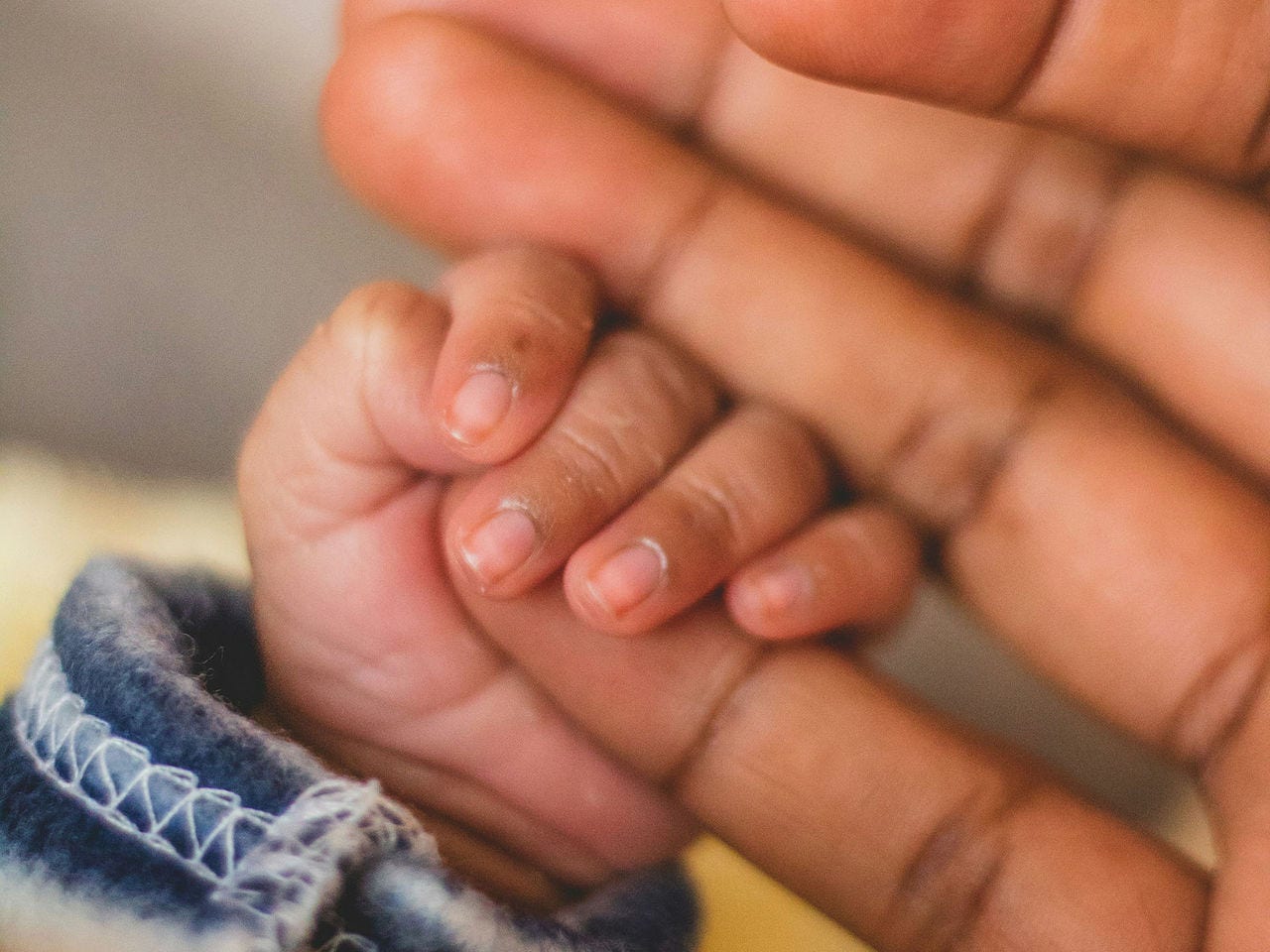 A baby hand holding its mother's finger