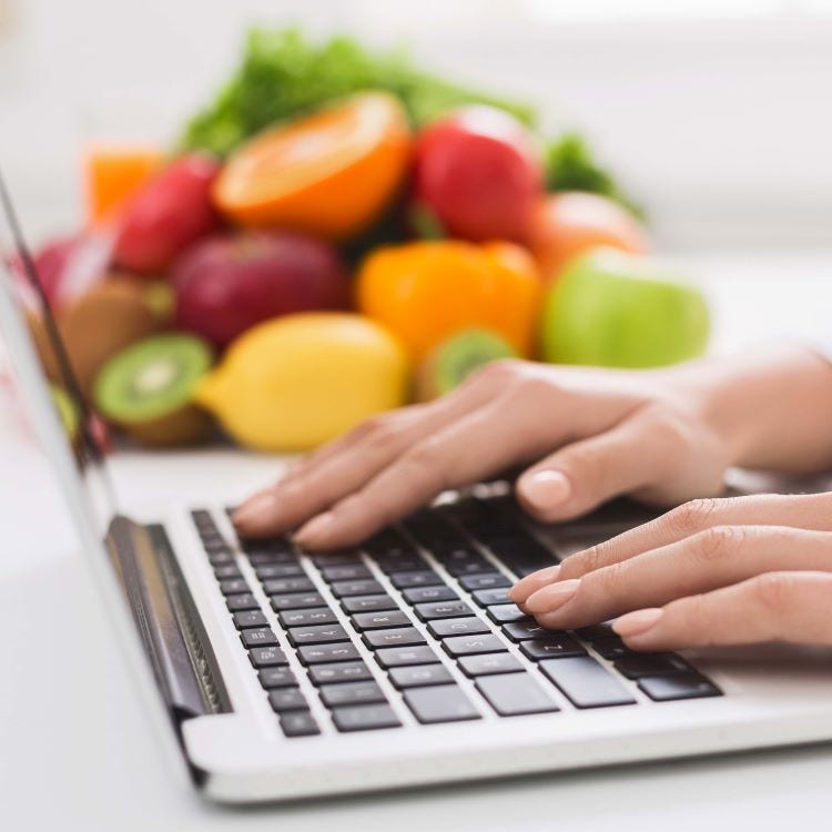 Stock photo of hands typing on a laptop with fruit in the background