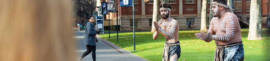 Indigenous dancers in traditional body paint performing outdoors on a university campus lawn