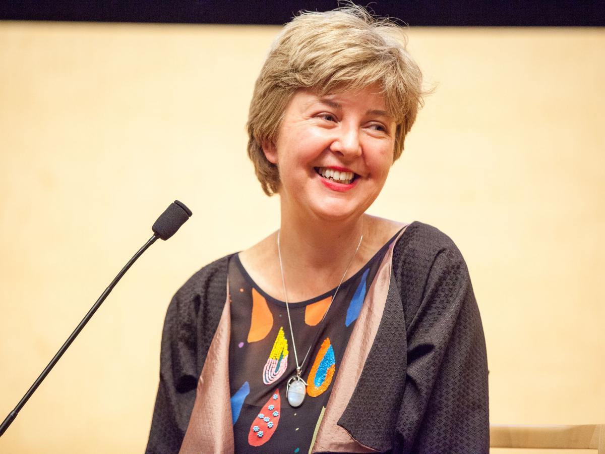 Jane Sloane wearing a colourful shirt and smiling, using a microphone