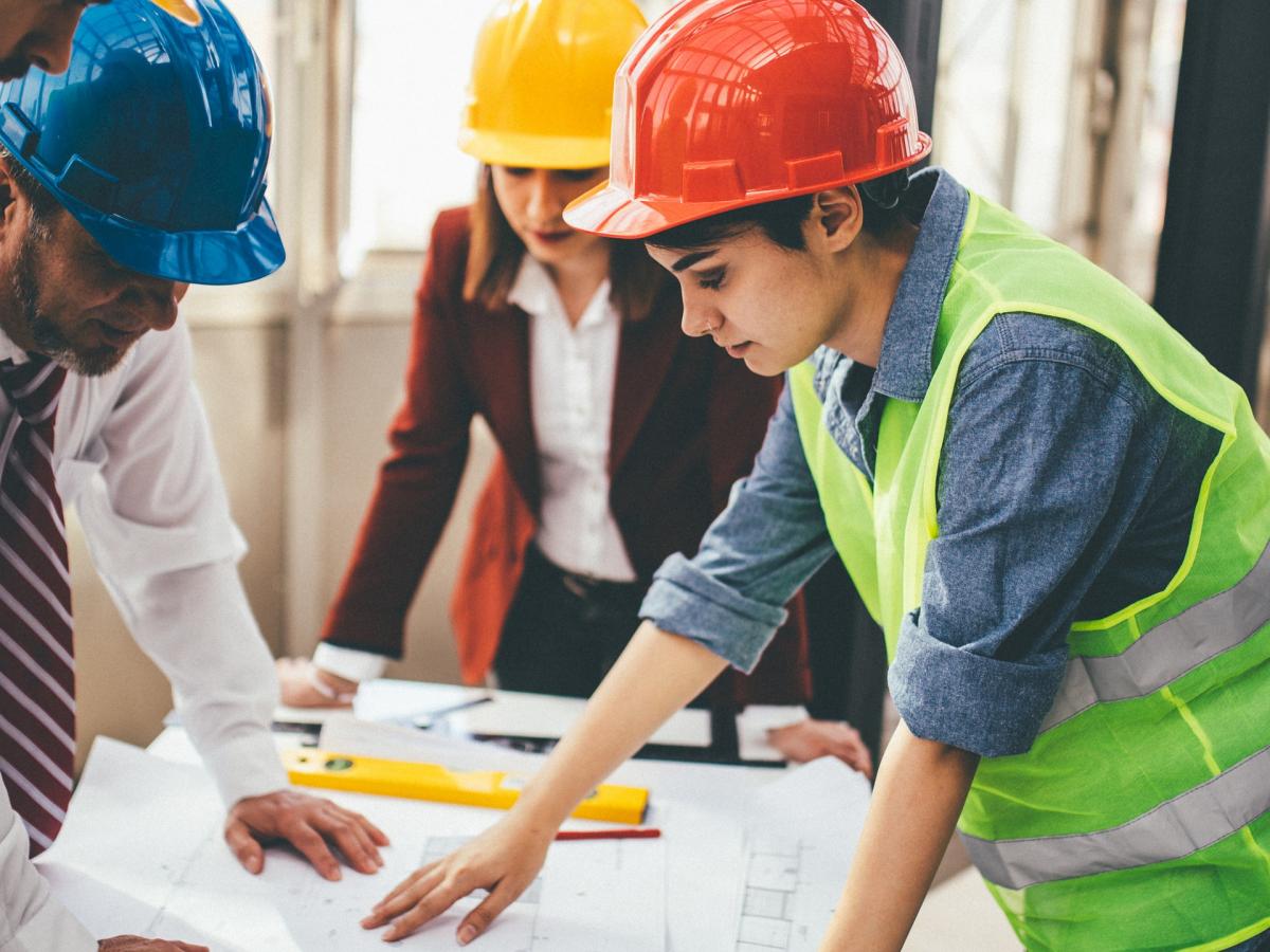 Three people in safety gear looking at building plans