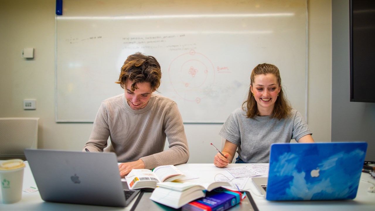 two students studying in a classroom with laptops