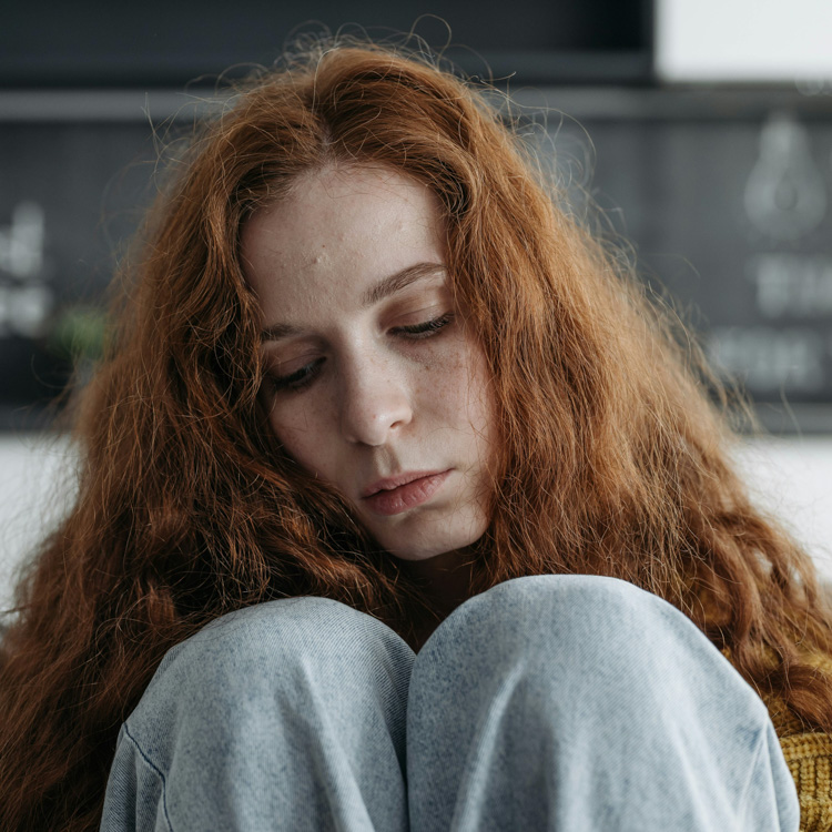 A woman with red hair sits on a couch looking sad.