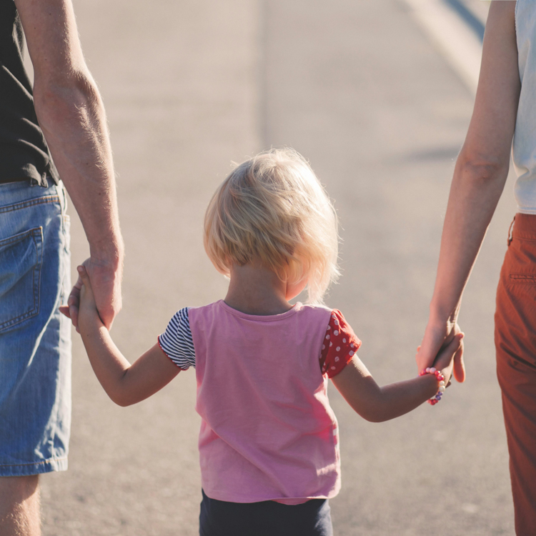 Child walking while holding hands with two adults