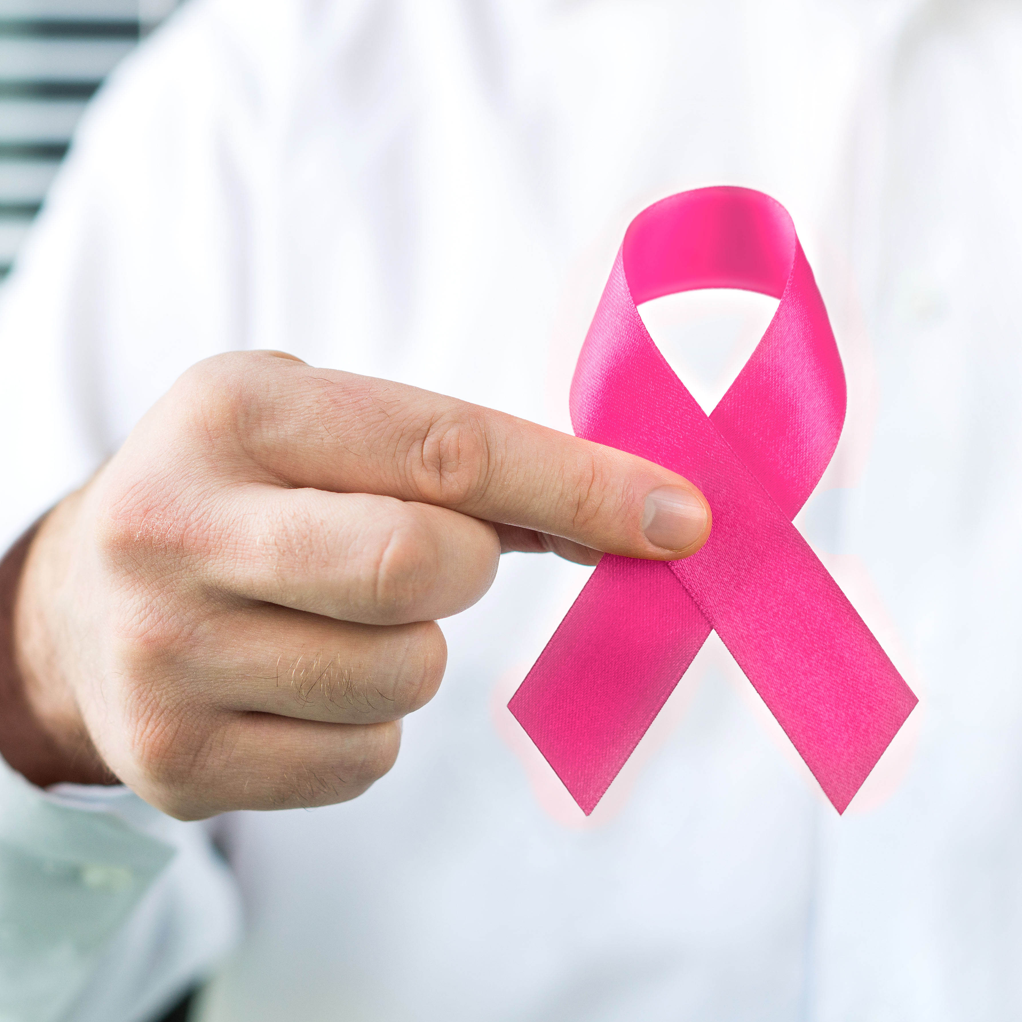 Hand holding pink ribbon to represent women's cancer