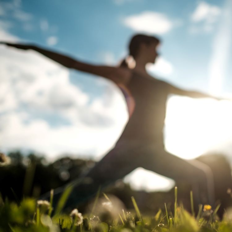 Blurred image of woman standing in a yoga pose in a grassy field.