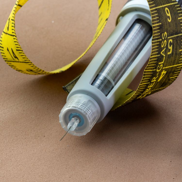 Stock image of a needle for diabetes medication surrounded by measuring tape..