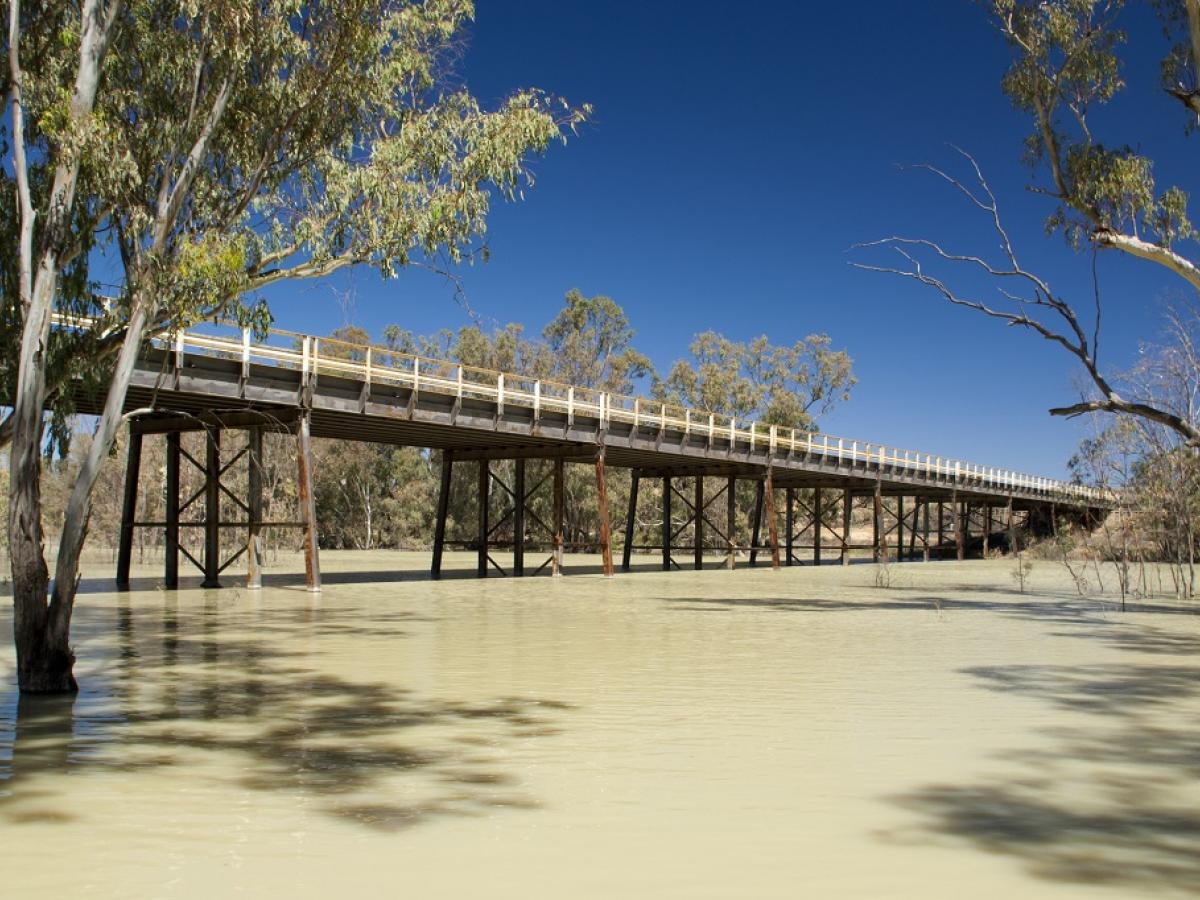 A bridge across the Darling River, trees are in the background with a blue sky above.