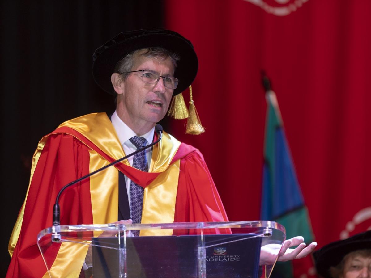 Peter Høj in graduation robes, speaking to an audiencee.