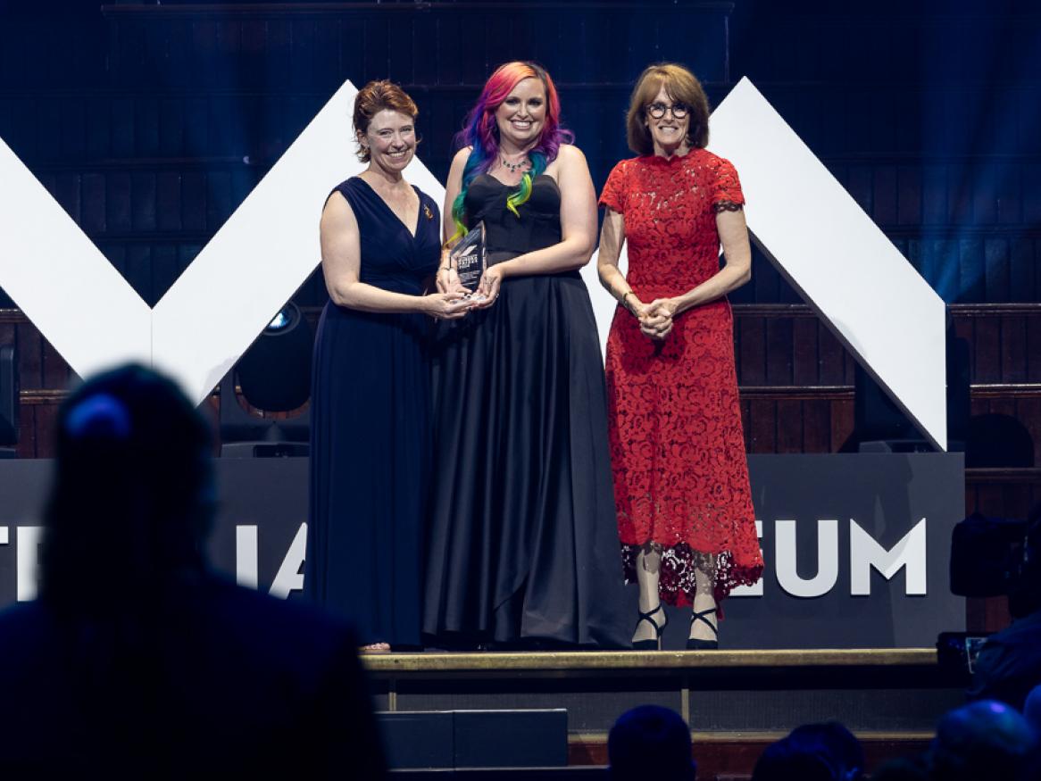 Three women stand on a stage with an award