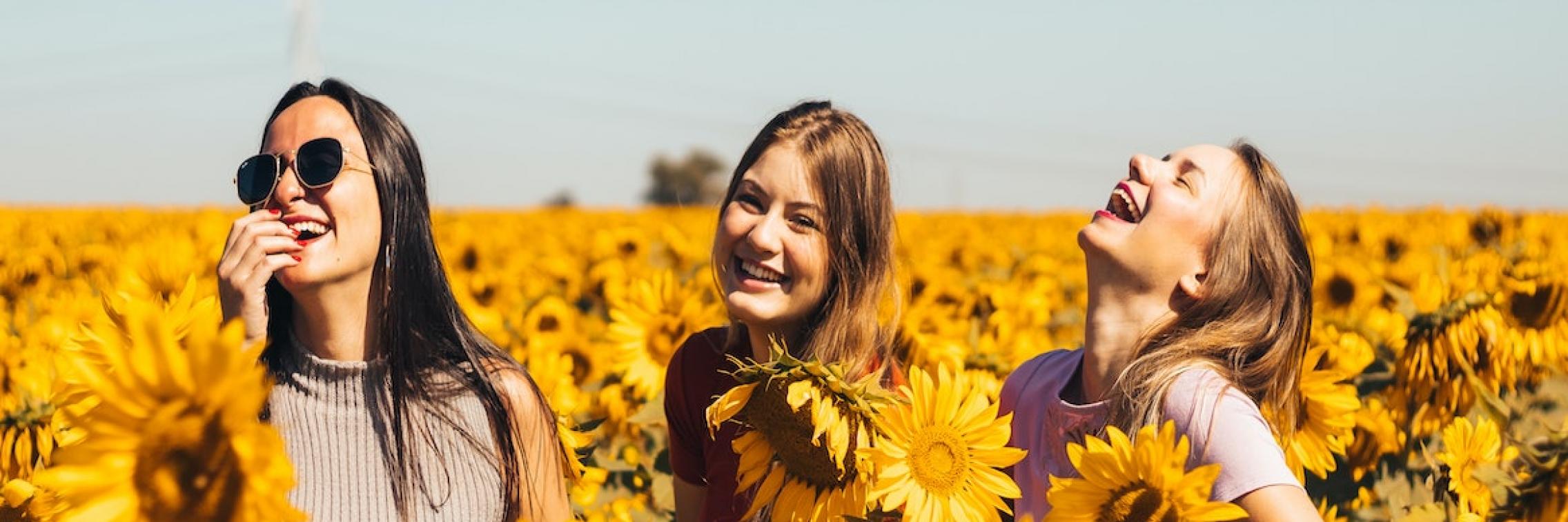 Three women laughing in a sunflower field.