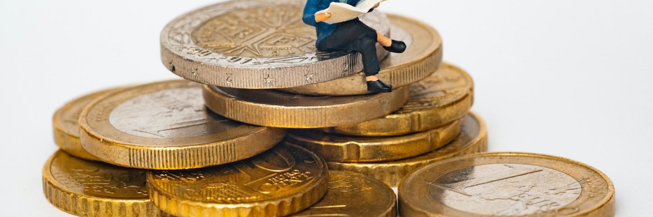 Miniature person sitting on large coins.