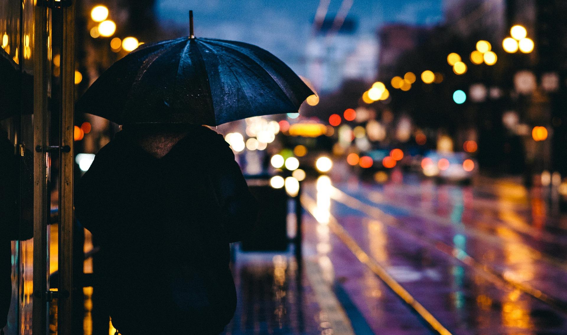 A person walks along a dark city street holding an umbrella