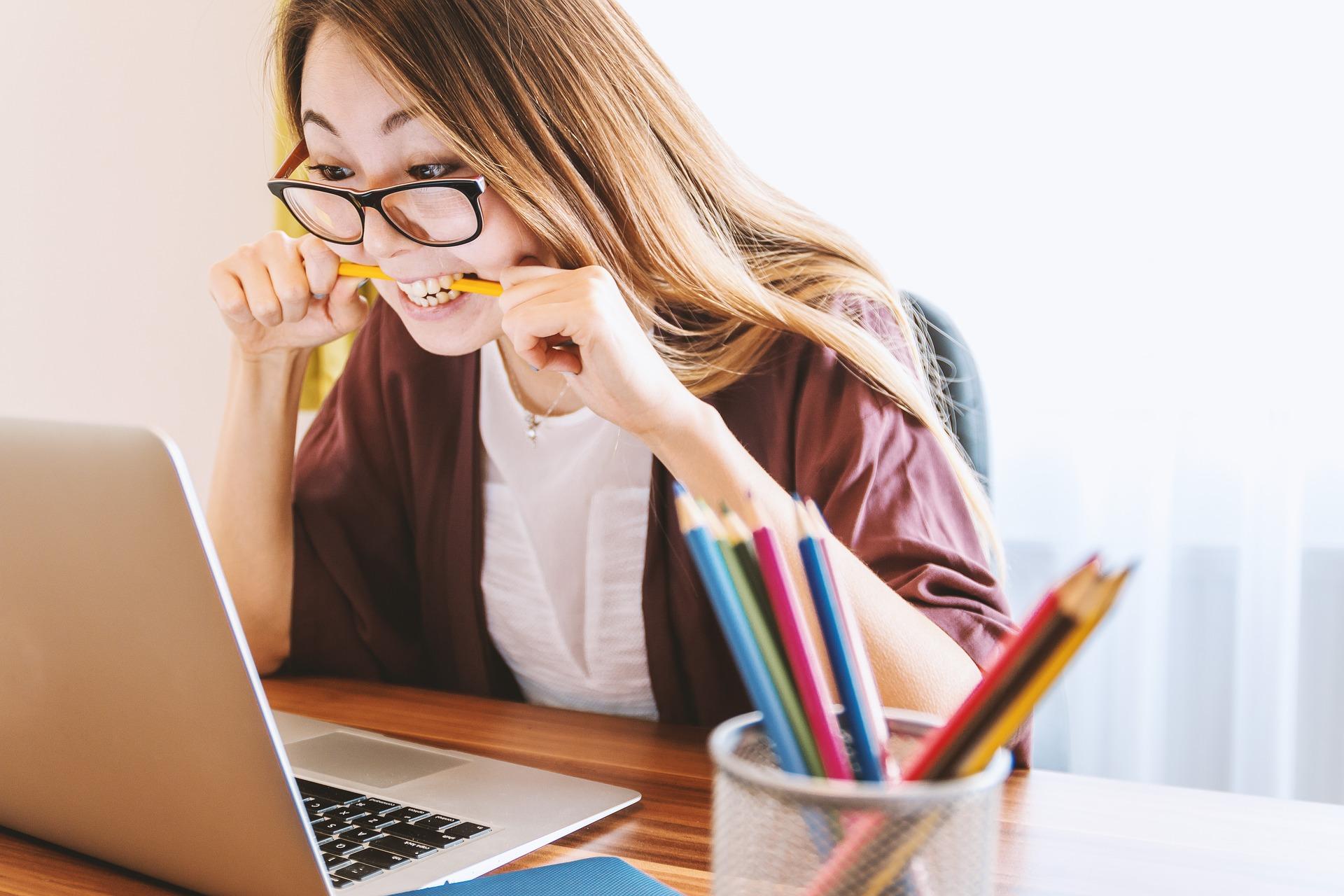 Girl chewing pencil on laptop