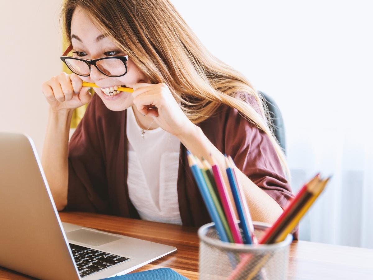 Girl chewing pencil on laptop