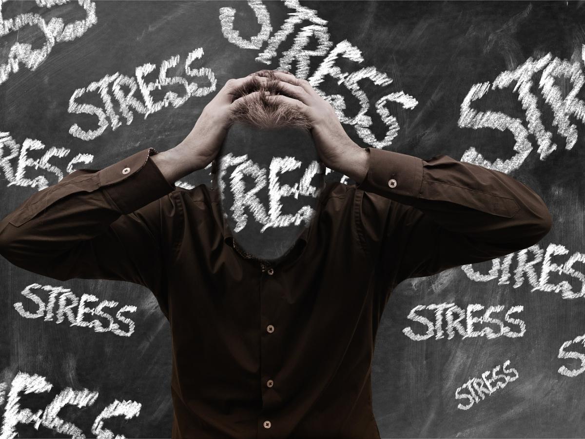 A man standing in front of a blackboard with the word stress in chalk everywhere including across their face.