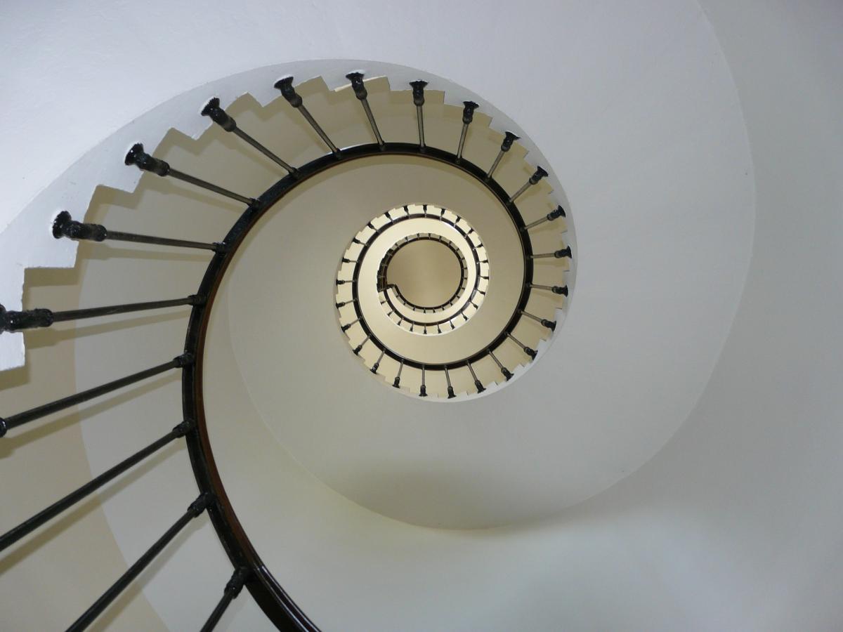 Looking at a white spiral stairway with dark wood railings from below. 