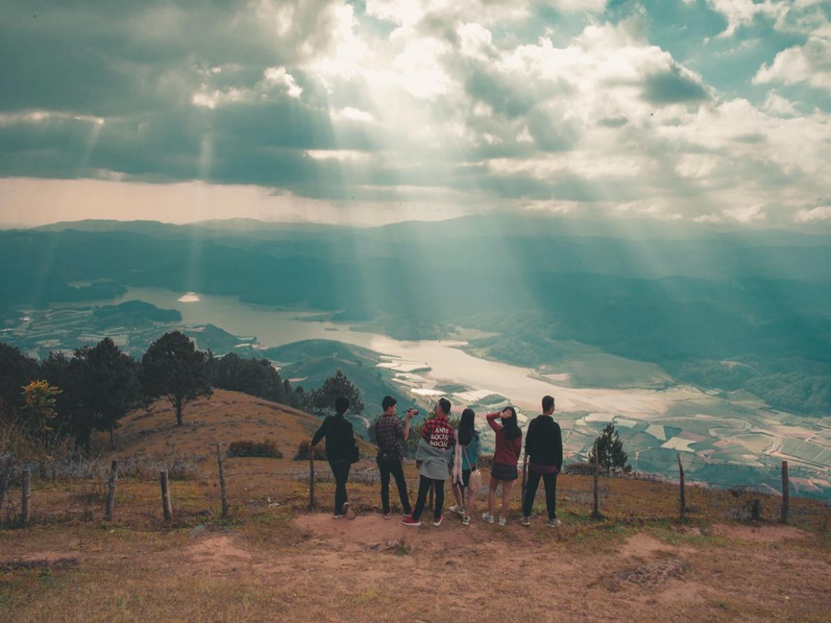 Six people standing in front of a great mountain and river view with the sun shining above them