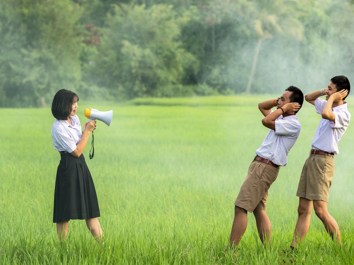 Lady with megaphone causes two men to put hands on ears