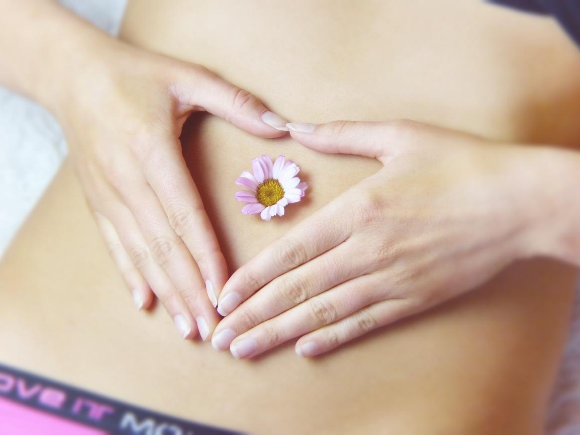 a woman making a heart over her stomach with her hands, a daisy rests in the middle