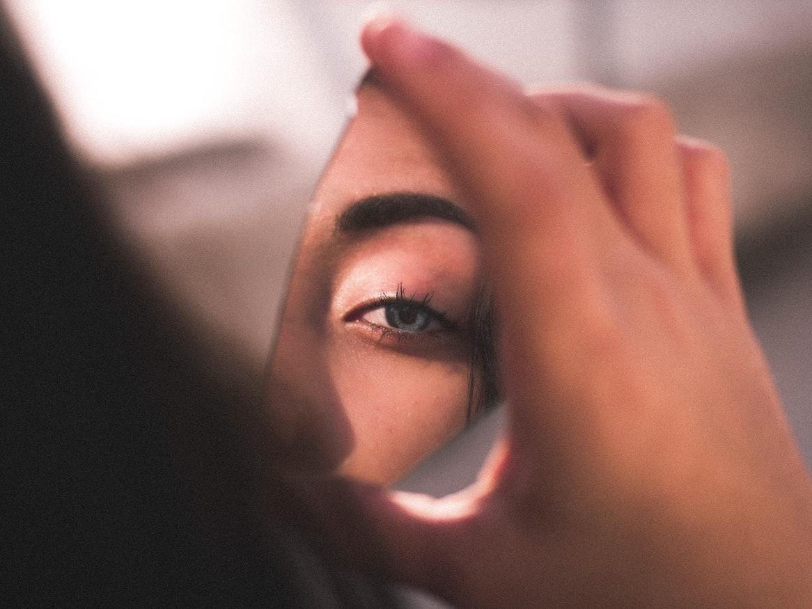 A young woman holding a mirror shard showing part of her face