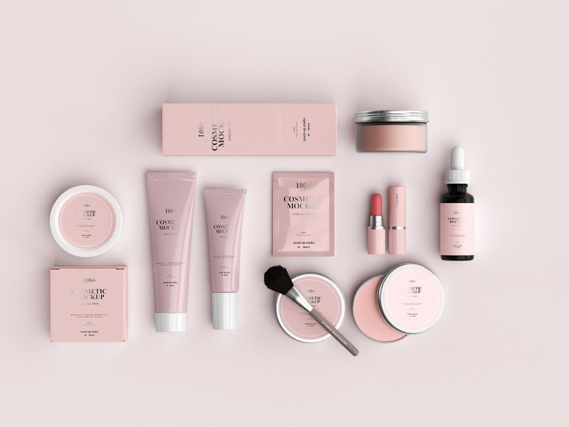 Various cosmetic products packed in light-pink tubes, boxes, compacts, and bottles spread across a light-pink background.