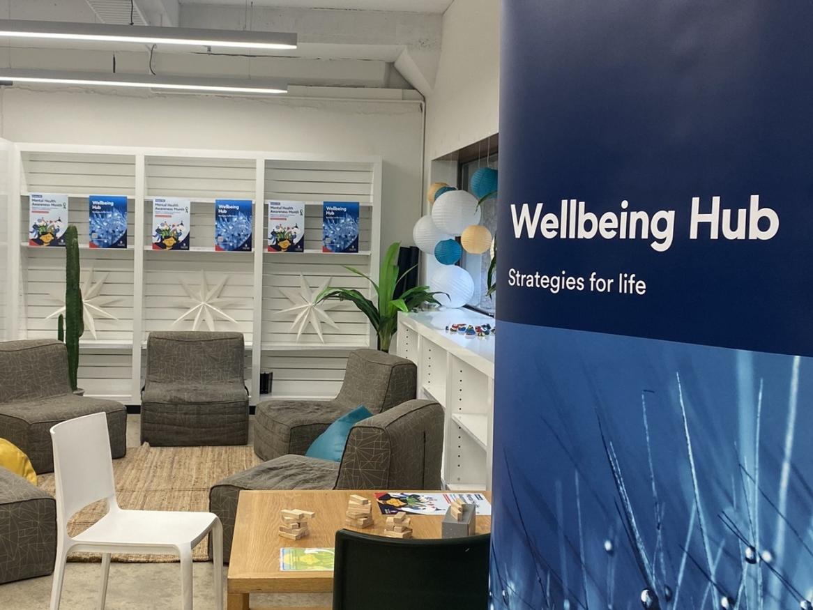 Photo of Wellbeing Hub banner, soft light brown chairs, posters, coloured lanterns and 2 plastic chairs