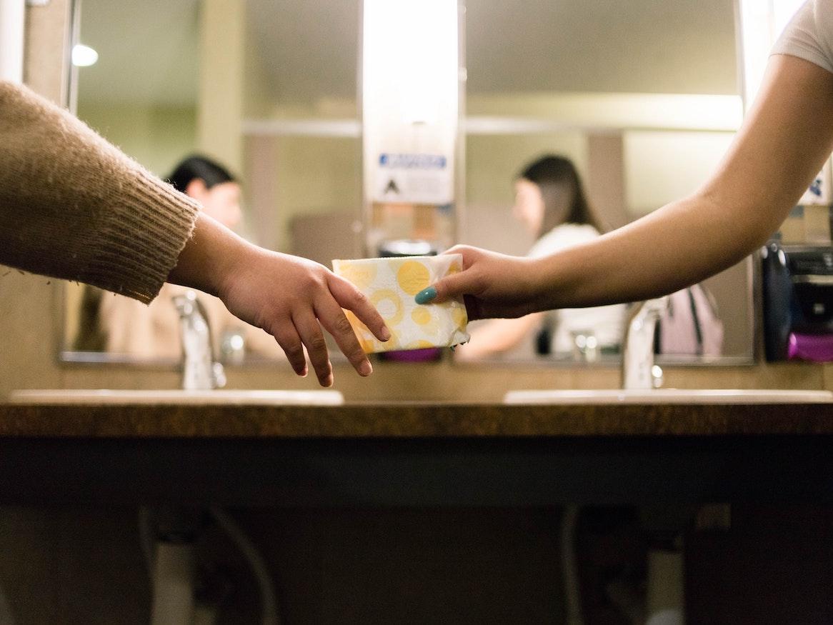 Person handing a sanitary pad to another person.