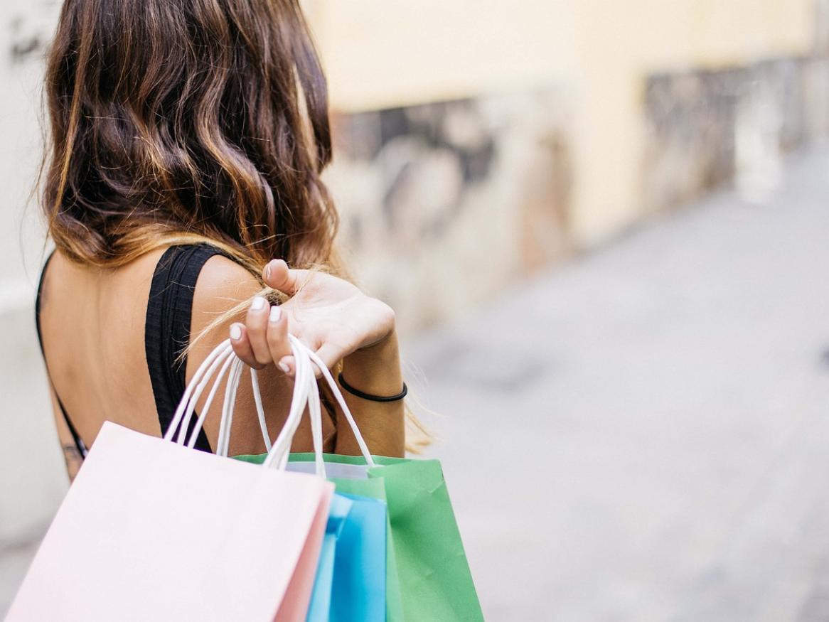 A woman, shown from the back, holding coloured shopping backs by the handle.