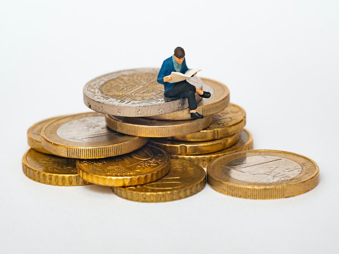 Miniature person sitting on large coins.