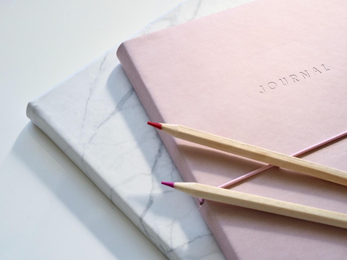 Two journals and two pencils stacked on a desk