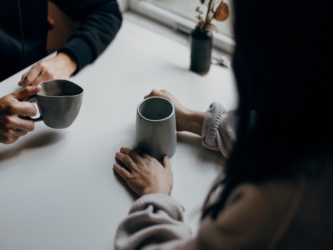 Two people holding ceramic mugs.