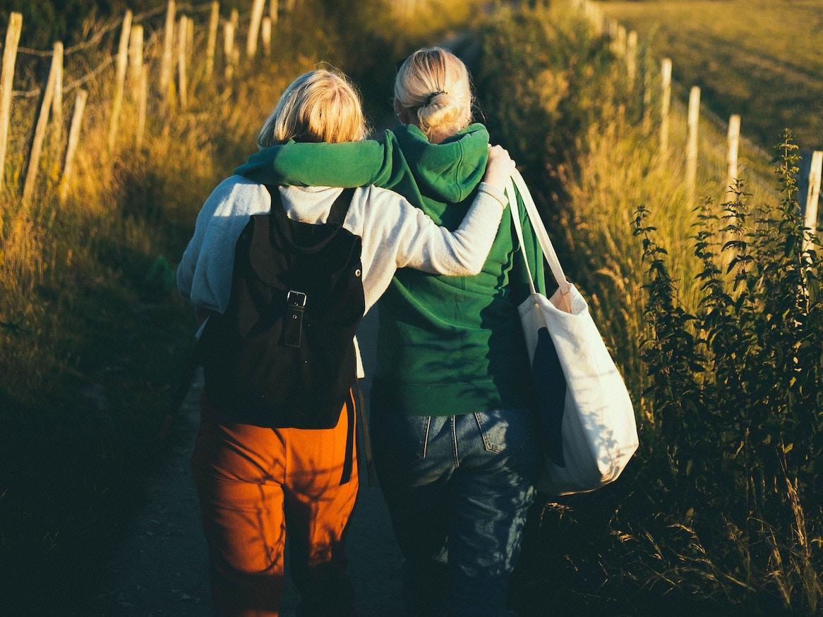 Two friends walking together on a path in a field.