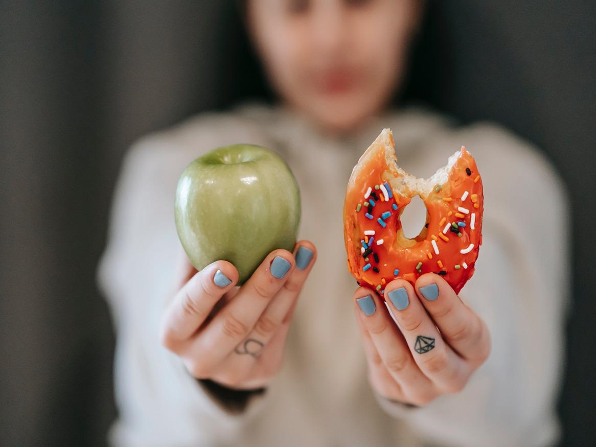 A woman holding an apple in one hand and a donut in the other