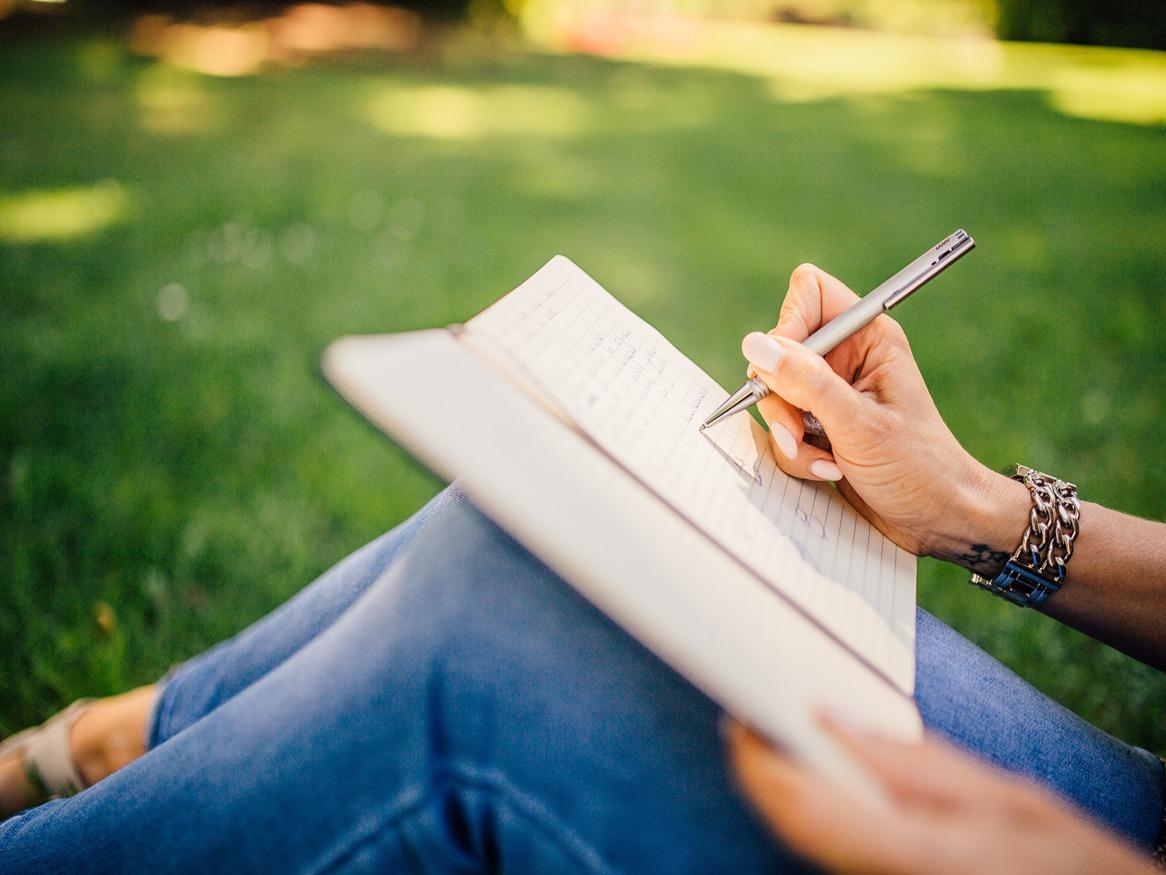 Someone writing in a journal while sitting on grass