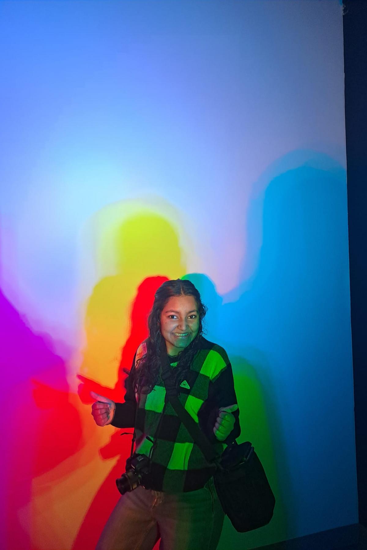 Portrait photo of Kanika in front of colourful rainbow walls