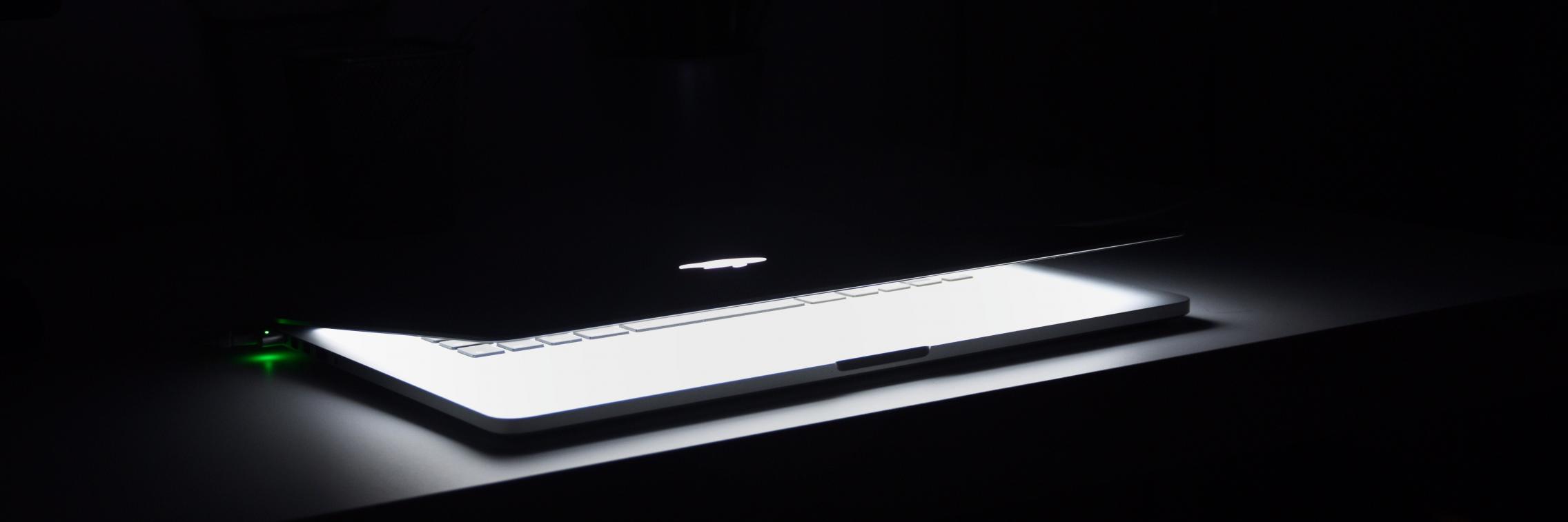 A partially-closed Mac laptop in the dark